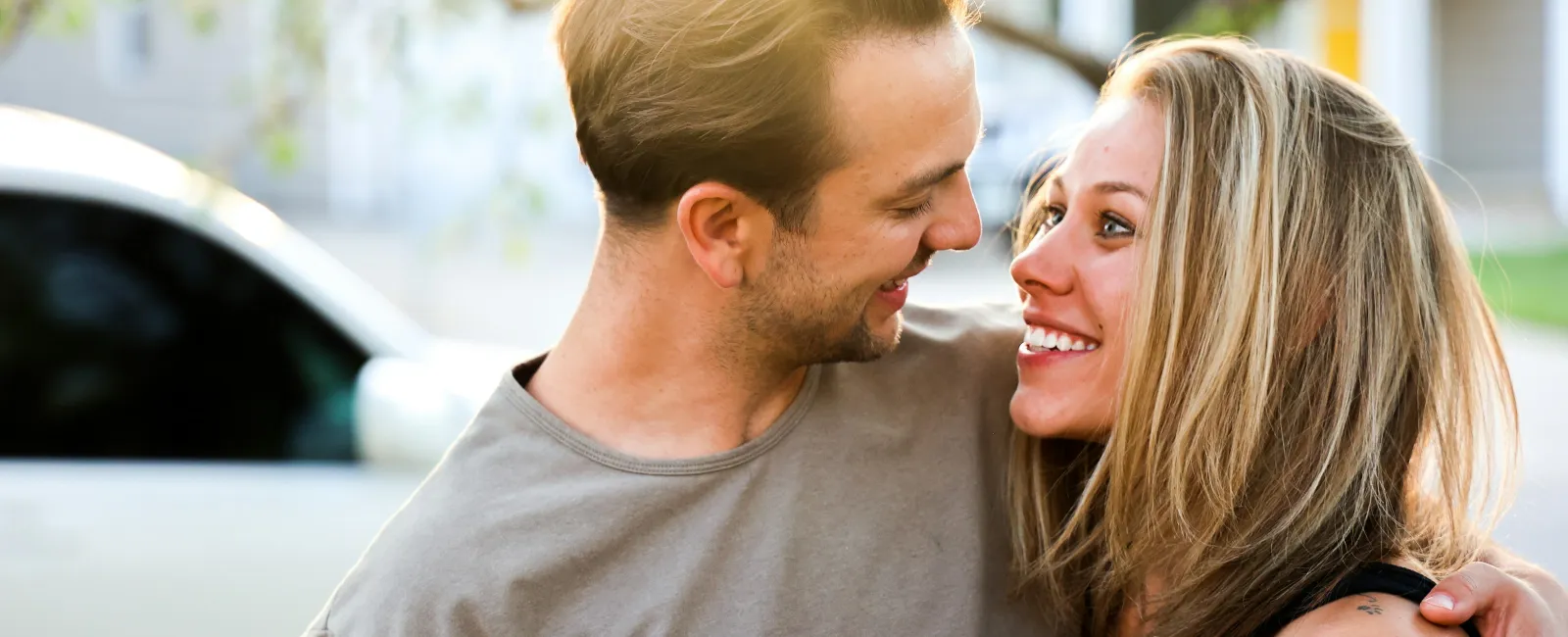 Happy young couple embracing and smiling at each other outdoors with a car in the background
