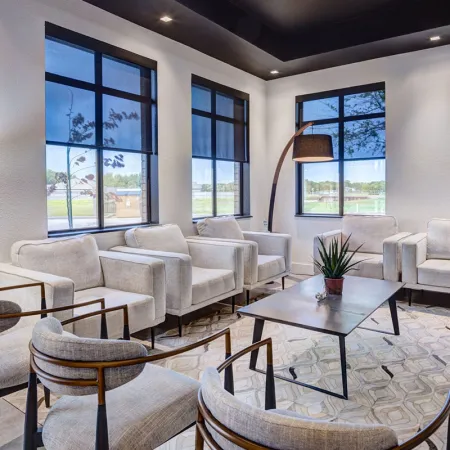 Modern living room with neutral armchairs, large windows, geometric rug, and black floor lamp in bright space.