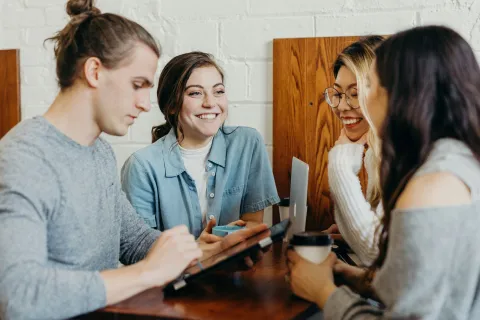 Group of young adults socializing and working together at a cafe with coffee and tablets.