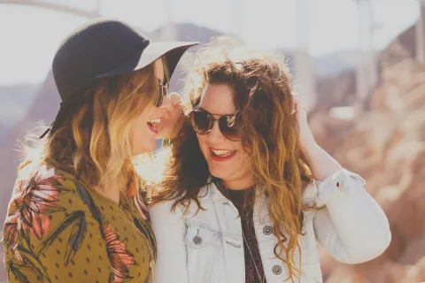Two women wearing sunglasses and smiling outdoors in a sunny, rocky environment