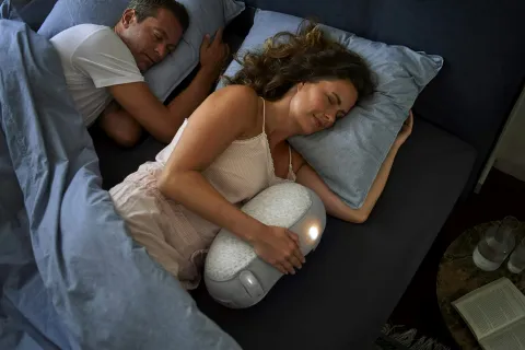 Couple sleeping in bed with woman holding a lighted heating pad or massager for comfort at night