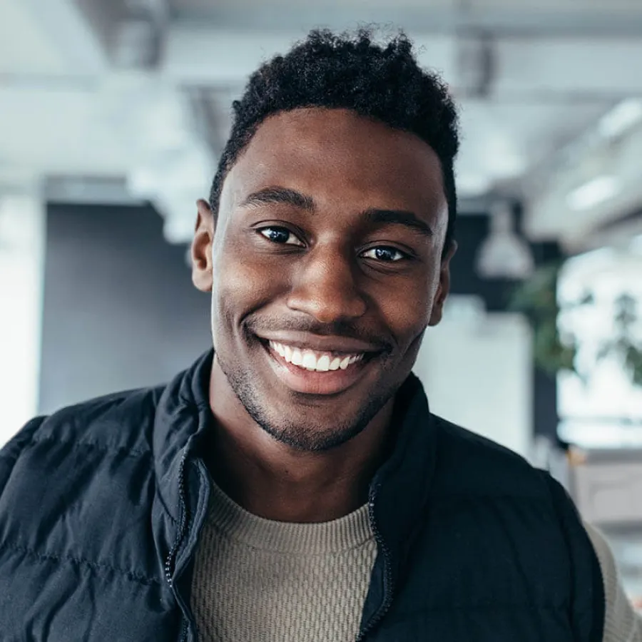 Smiling young African American man wearing a black jacket in a modern indoor setting with natural lighting.