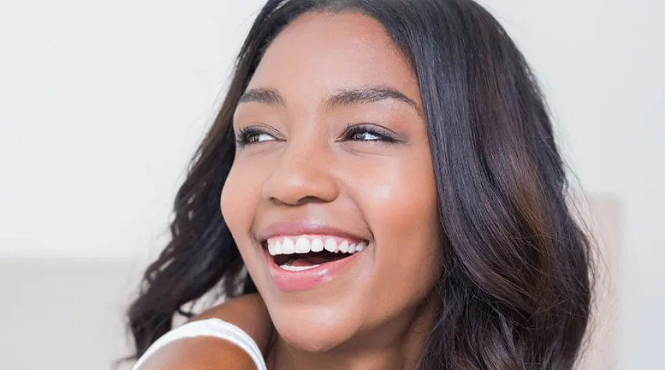 Smiling young woman with long wavy hair looking to the side in bright natural light indoors.