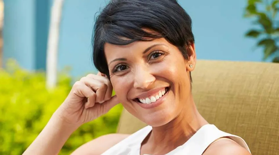 Smiling woman with short hair relaxing in a sunny garden setting on a cozy chair.
