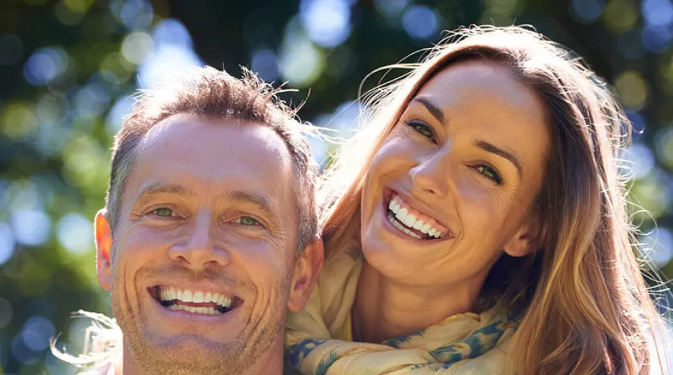 A joyful couple smiling together outdoors, showcasing happiness and connection in a sunny environment.
